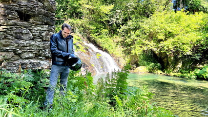 a beautiful frazz stands against the backdrop of a waterfall he leaned against the stone wall of a dilapidated building and looks into the distance peace there is a place for text.