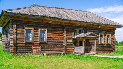 An old house in the village made of dark logs with a wooden roof. Summer flowers in front of the house in the countryside. Wooden old manor house of the 19th century. Clean air in the village