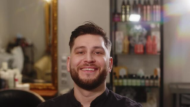 Handsome young happy man smiling after haircut while sitting in chair in barbershop