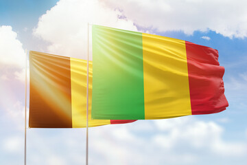 Sunny blue sky and flags of mali and belgium