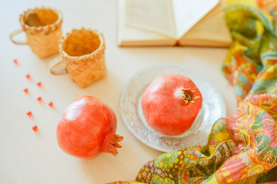 Whole pomegranates in plate, opened cookbook, vitamins and cups on the table