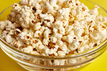 Large transparent bowl filled with popcorn on a yellow background.
