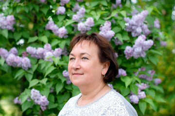 portrait of an attractive mature woman 50-60 years old on a blurry background of beautiful lilac bushes, travel and retirement