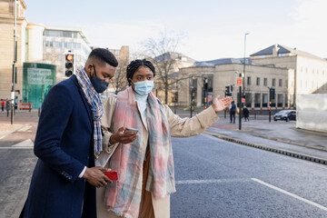 Couple Wearing Face Coverings Hailing Cab Using Phone