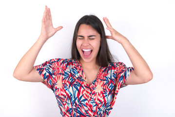 young beautiful brunette woman wearing colourful dress over white wall goes crazy as head goes...