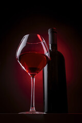 Bottle and glass of red wine on a dark background