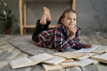 smiling little student girl with book lying on the floor, schoolgirl with books looking at camera...
