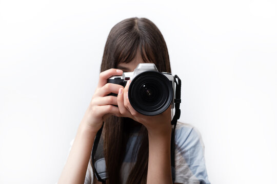 Teenage young woman taking pictures on professional camera. Portrait of a teen israeli photographer covering her face with the camera. White background
