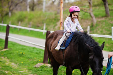 Small baby girl in pink helmet ride pony.