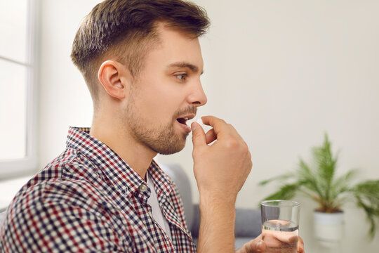 Man who has a health condition is taking medication prescribed by his doctor. Side profile closeup view of a handsome young Caucasian man taking a pill and drinking a glass of water. Medicine concept