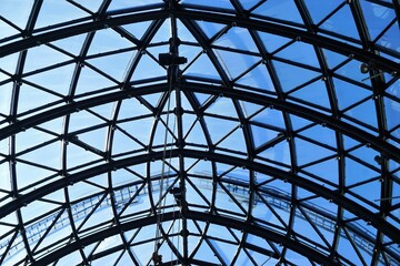 Glasdach mit Rundbogengitter aus schwarzem Stahl vor blauem Himmel bei Sonne im Fr&uuml;hling