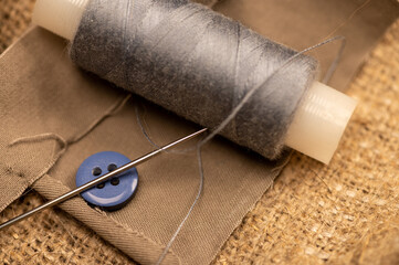 A spool of sewing thread and a sewing needle on a fabric background. Close-up, selective focus