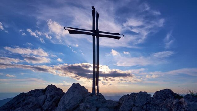 Christian cross on a rock. Clouds in the blue sky lit by the setting sun are slow moving.