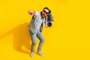 Fototapeta premium Photo of cool sweet man wear jeans waistcoat arm dark eyewear listening boom box pointing you isolated yellow color background