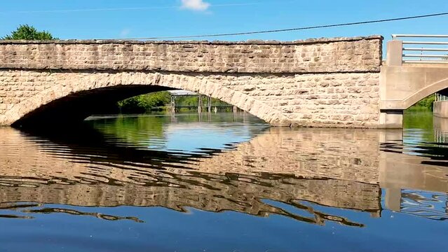 Contrasting historic bridge with modern extension with dam in background.