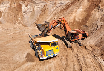 Excavator load sand into mining truck in opencast. Mining excavator in open pit during sand mining. Excavator on development sand pit. Earth Mover load soil in haul truck. Earthmover on sand mining.