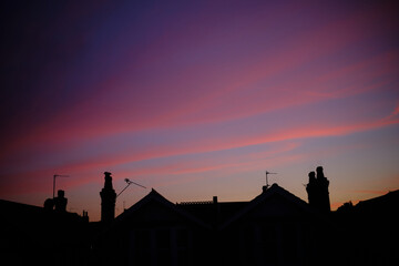 Rooftops silhouetted against a vibrant purple and blue sunset sky.