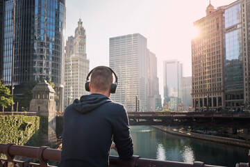 Rear view of pensive man with wireless headphones during city walk. Chicago cityscape, United States..