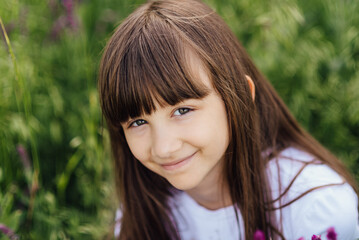 Cute little girl 7-8 years old, sitting in the lavender field, looking at the camera and smiling, close portrait