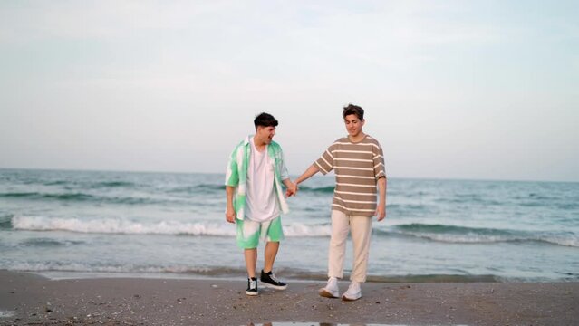 Happy Young Gay Couple Walking Along The Beach Together