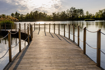 Fototapeta premium Long Wooden bridge over lake. Beautiful sunrise over lake pier. Planked footway on the river