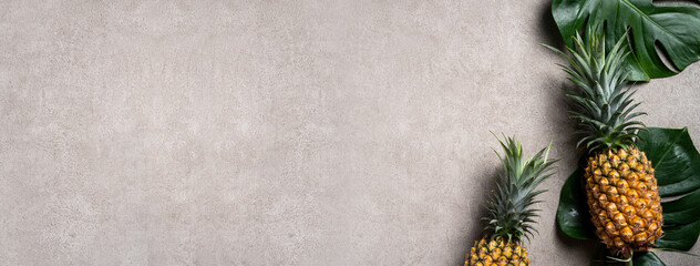 Fresh pineapple with tropical leaves on gray background.