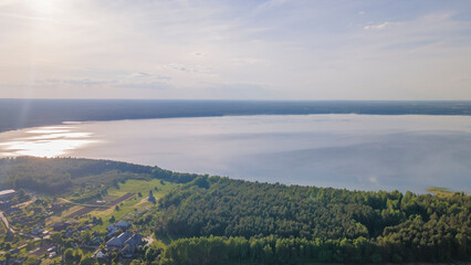 Aerial view of lake and small village on the peninsula. Sunset evening light by calm water on warm beautiful summer day.