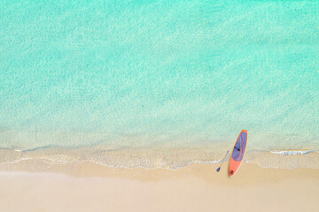 Fototapeta na wymiar Top view of tropical Seychelles sand beach with SUP board for surfing on the shore. Blue, turquoise transparent water surface of ocean, sea, lagoon. Horizontal background. Aerial, drone view