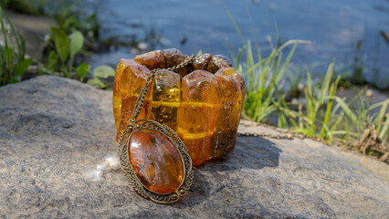 Beautiful big orange amber pendant and bracelet on a stone near the river. Slavic culture. 
