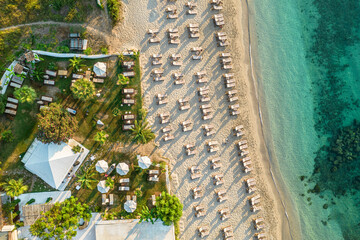 Fototapeta premium Aerial view of many white sunbed, lounge on sandy beach. Summer and travel concept. Blue, turquoise transparent water surface of ocean, sea, lagoon. Aerial, drone view
