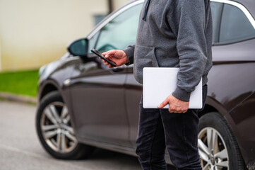 a silhouette of a man with a computer and a phone in his hands on the background of a parked vehicle