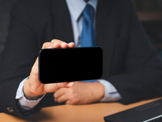 Businessman in a suit holding a blank screen smartphone while sitting in the office