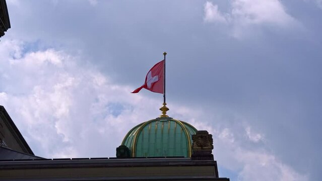 Swiss flag waving at Federal Palace of Switzerland (German Bundeshaus), residence of national Swiss government and parliament. Slow motion movie shot June 16th, 2022, Bern, Switzerland.