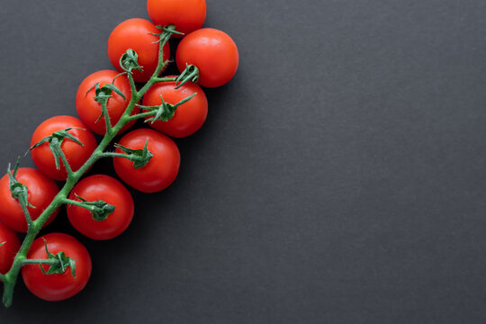 Top view of natural cherry tomatoes on branch on black surface with copy space.