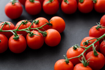 Close up view of fresh cherry tomatoes on branches on black background.