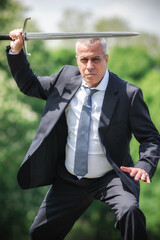 Portrait of handsome businessman model man in a modern casual suit with a large medieval sword. Modern fashion street style concept. Elegant urban warrior. Corporate and money security