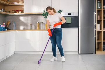 Woman in red gloves is doing housekeeping and sweeping floor in a kitchen