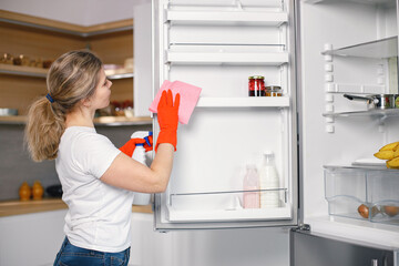 Woman in red gloves is doing cleaning and wash a refrigerator inside