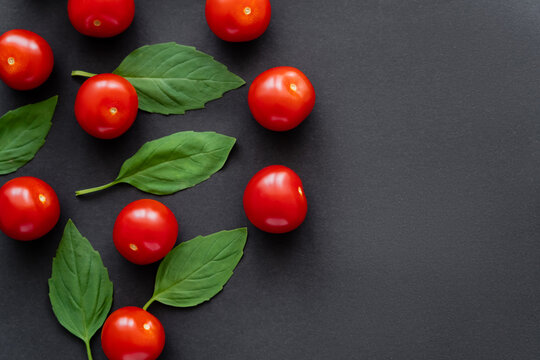 Top view of fresh basil and cherry tomatoes on black background.