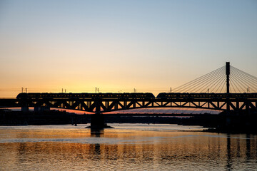 Fototapeta na wymiar The train riding over the bridge over the river at sunset.