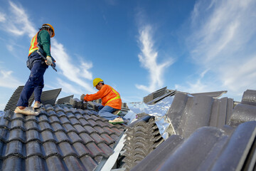 Asian male roof installer Asian construction workers on the roof Work using a drill bit to fix...
