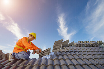 male roof installer construction workers on the roof working Use a drill bit to fix ceramic or cement tile roofing screws at the construction site.