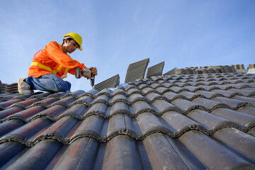 A male roofing installer is working on the roof of a house. Construction workers repair the roof of a house using drills and screws.