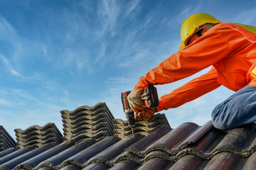 A male roofing installer is working on the roof of a house. Construction workers repair the roof of...
