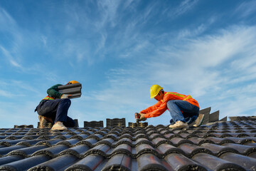 Two male roofers stand on the roof. Construction workers repair the roof of a house using drills...
