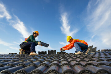 Asian male roof installer Asian construction workers on the roof Work using a drill bit to fix...