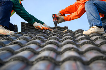 Close-up photo of a roofer working on the roof of the house Use a drill to drill the screws to fix...