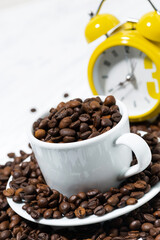 cup with coffee beans and an alarm clock, conceptual photography on white background, vertical top view