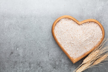 Wheat flour in a wooden heart shape bowl on a pastel background.