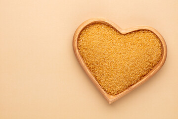Brown sugar in heart wooden bowl shape on pasttel background.
